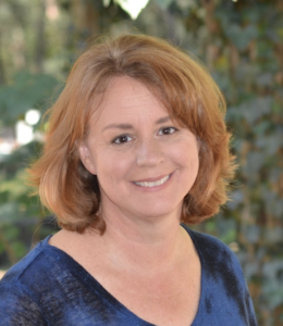 Headshot of Professor Lynn Ramey. Subject is wearing a blue shirt and the photo was taken outdoors.