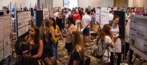 A crowd gathers between rows of posters at the Undergraduate Research Fair.