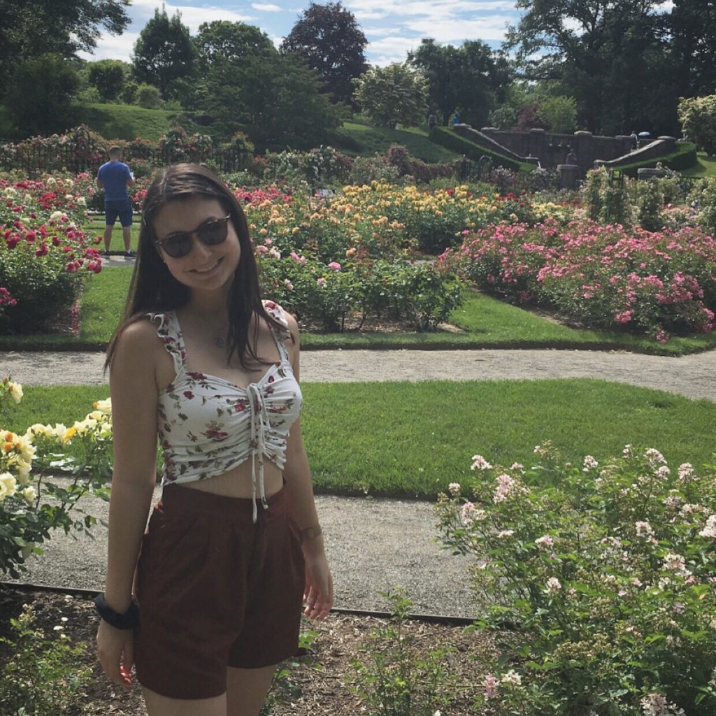 Nicole Gillis standing among many colorful flowerbeds outside on a sunny day