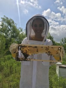 Young woman wearing beekeeper suit, holding honeycomb