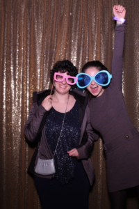 Alyssa Levitt poses for a photo with another student, wearing large, colorful glasses. In the photo, Alyssa punches her hand in the air in excitement.