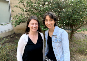 Two women standing in front of a bush smiling