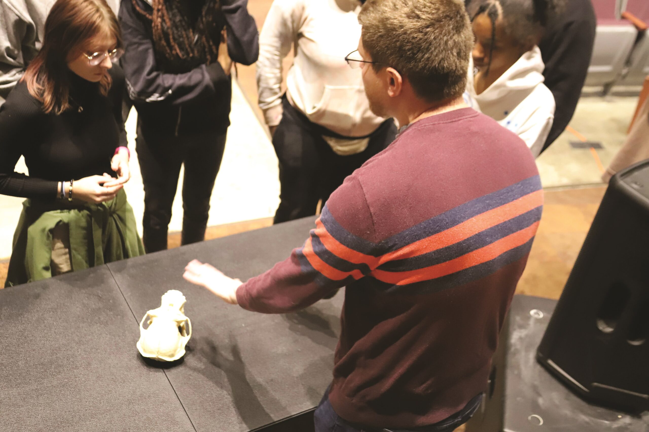 Kyle in a red sweater behind a black table with four students gathered around