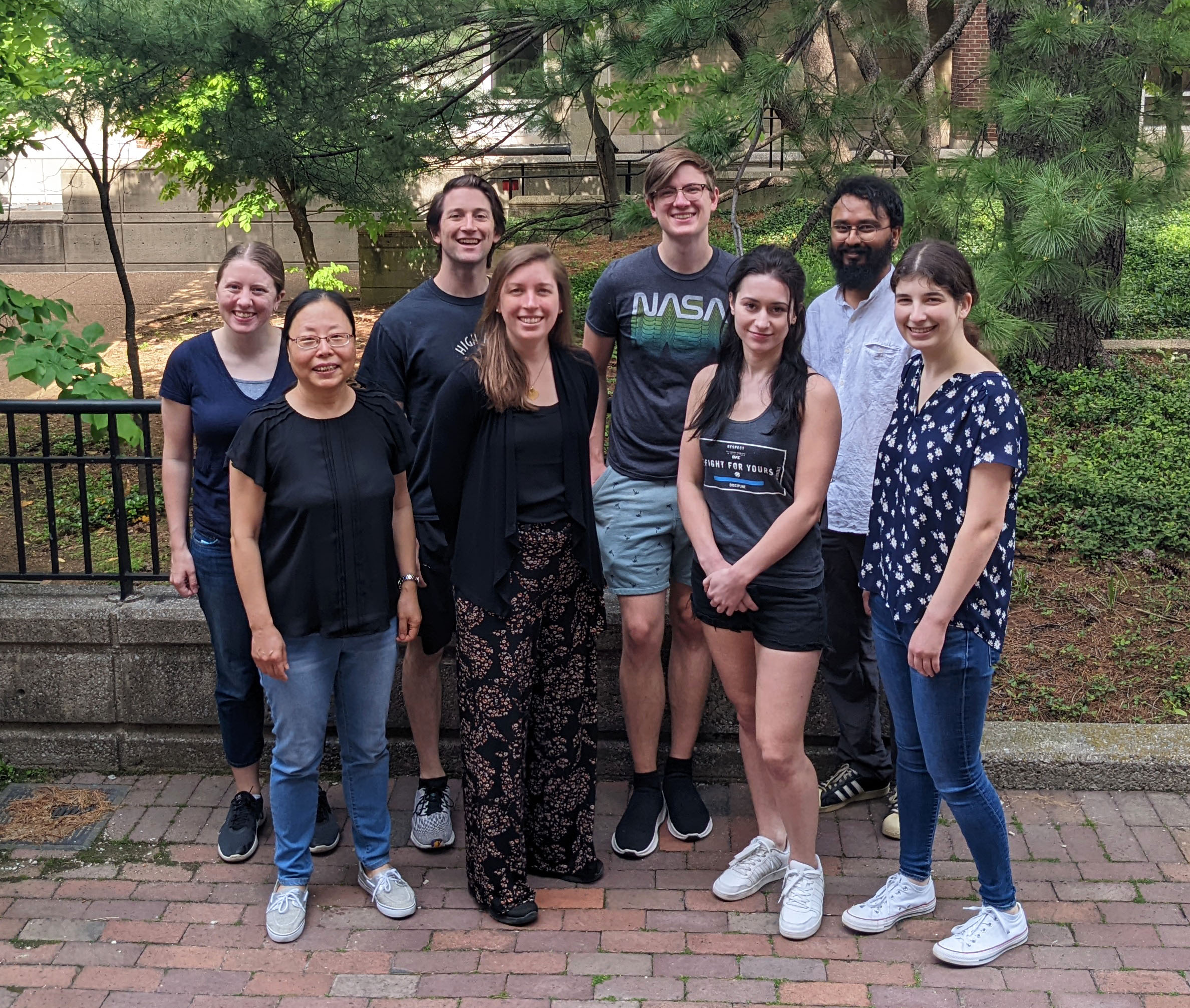 Members of the Tate lab standing in front of a tree on a brick sidewalk all smiling.