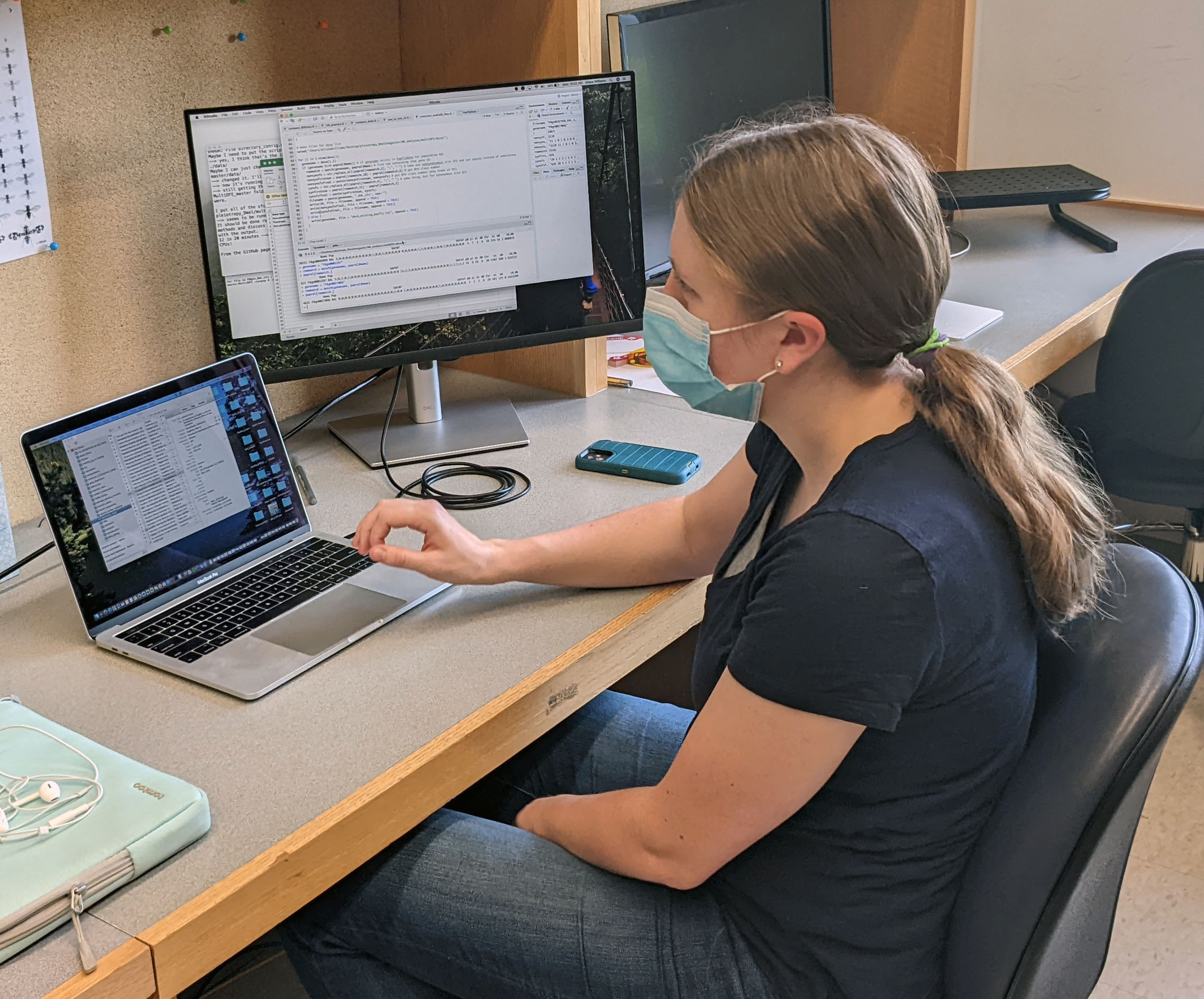 Alissa at a desk in a blue shirt and blue jeans working on some code