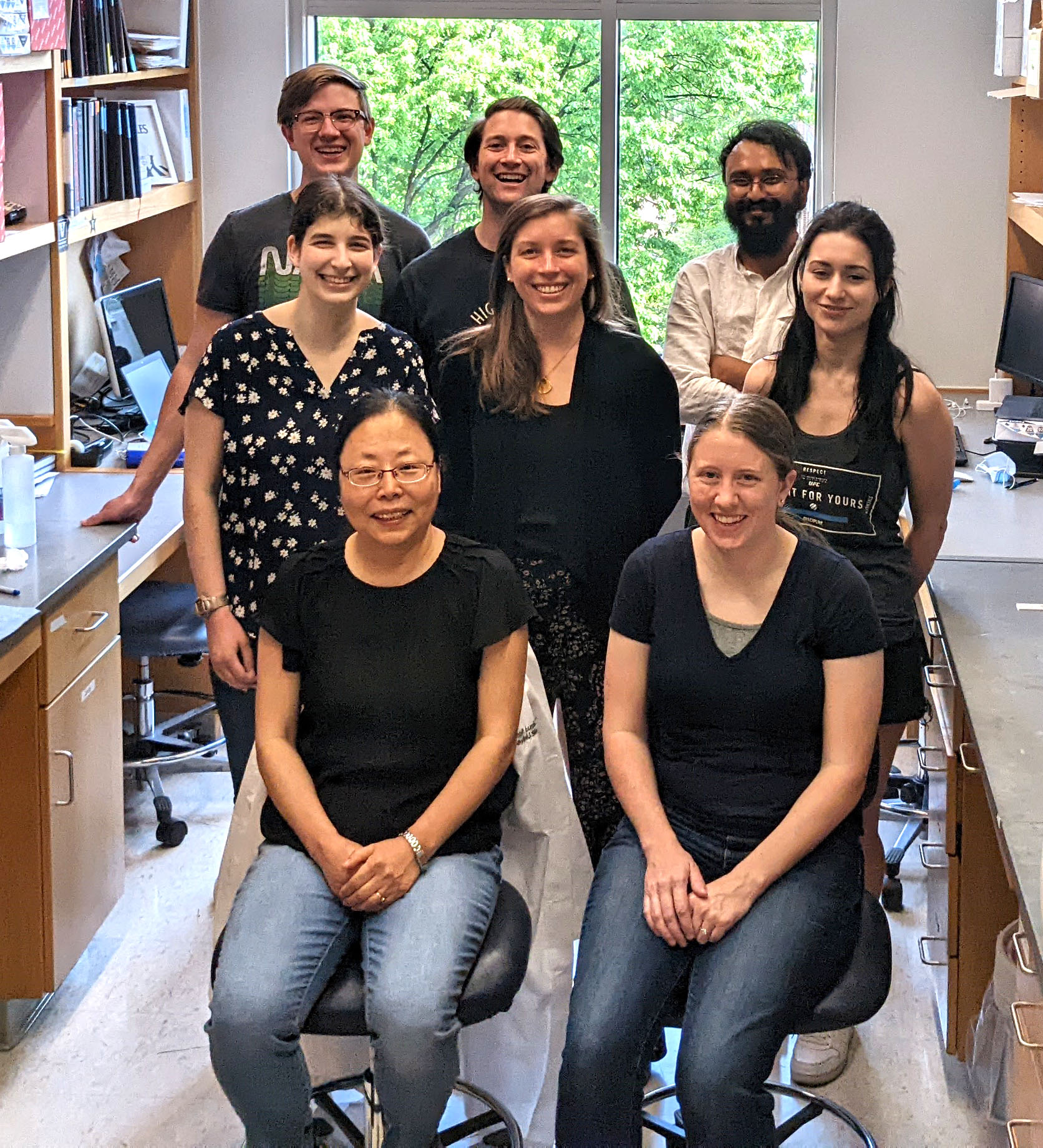 Thi Ngo front left and Alissa front right sitting with other members of the Tate lab in front of a window. Everyone smiling