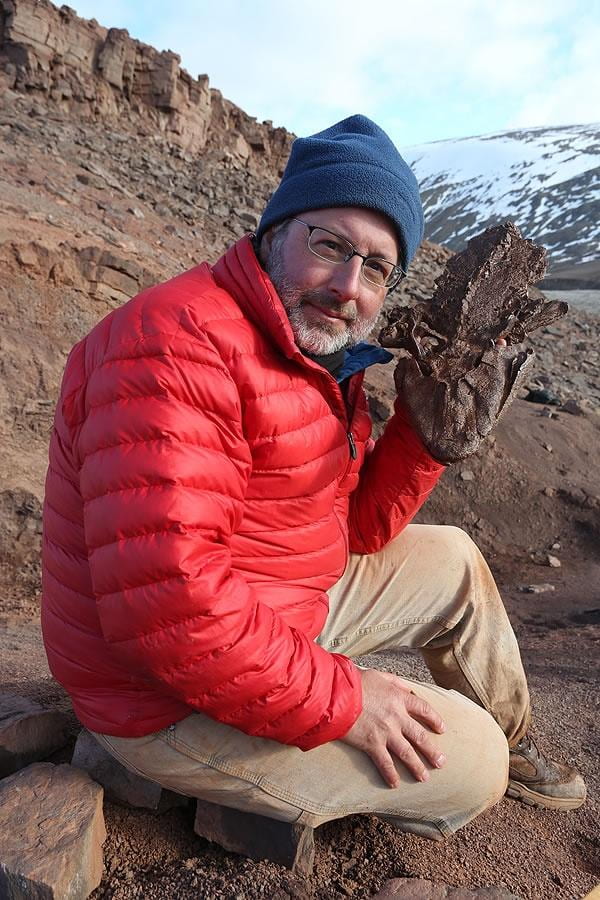Neil in a blue hat and red coat holding a fossil of Tiktalik