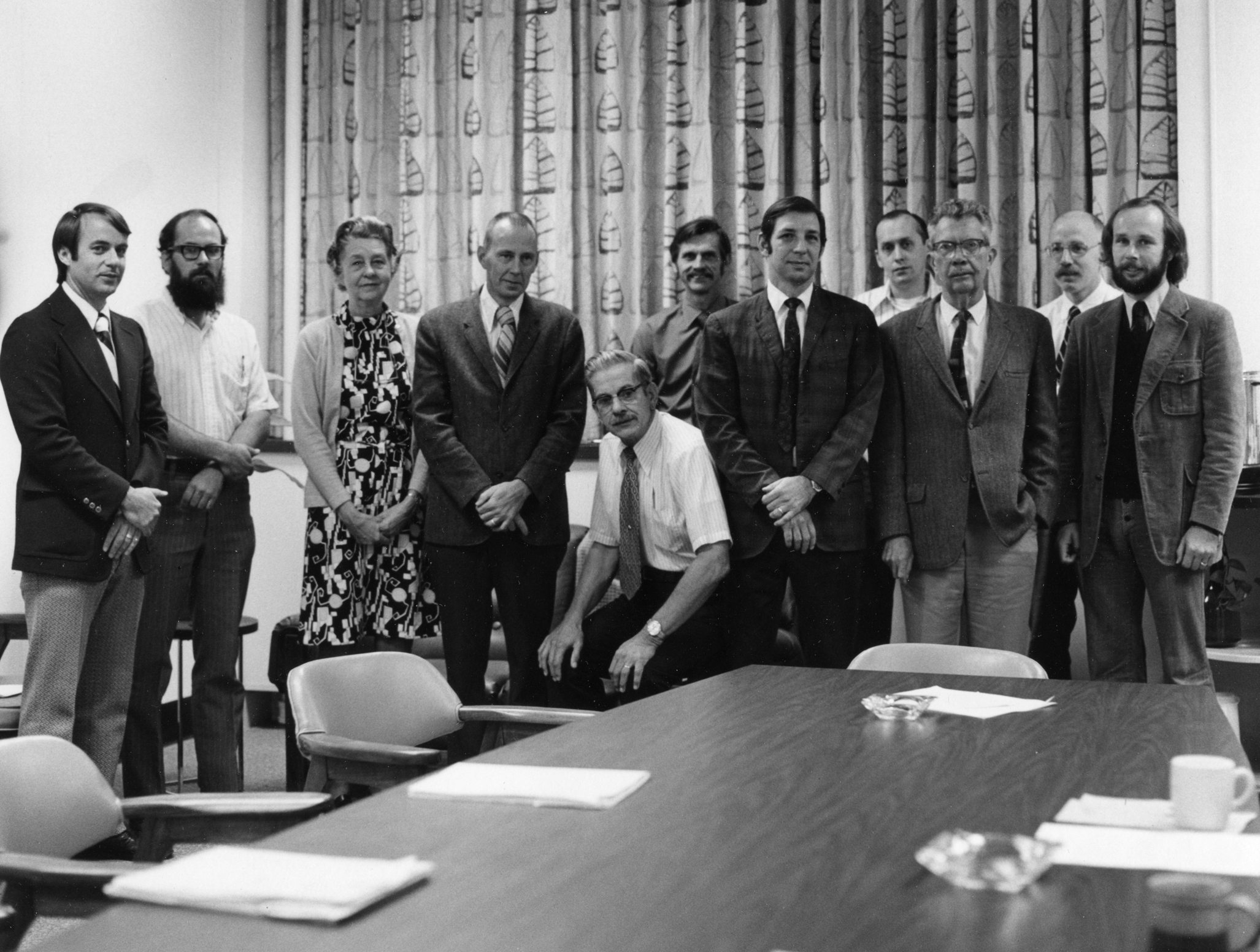 A greyscale photo of the biology faculty standing around a table