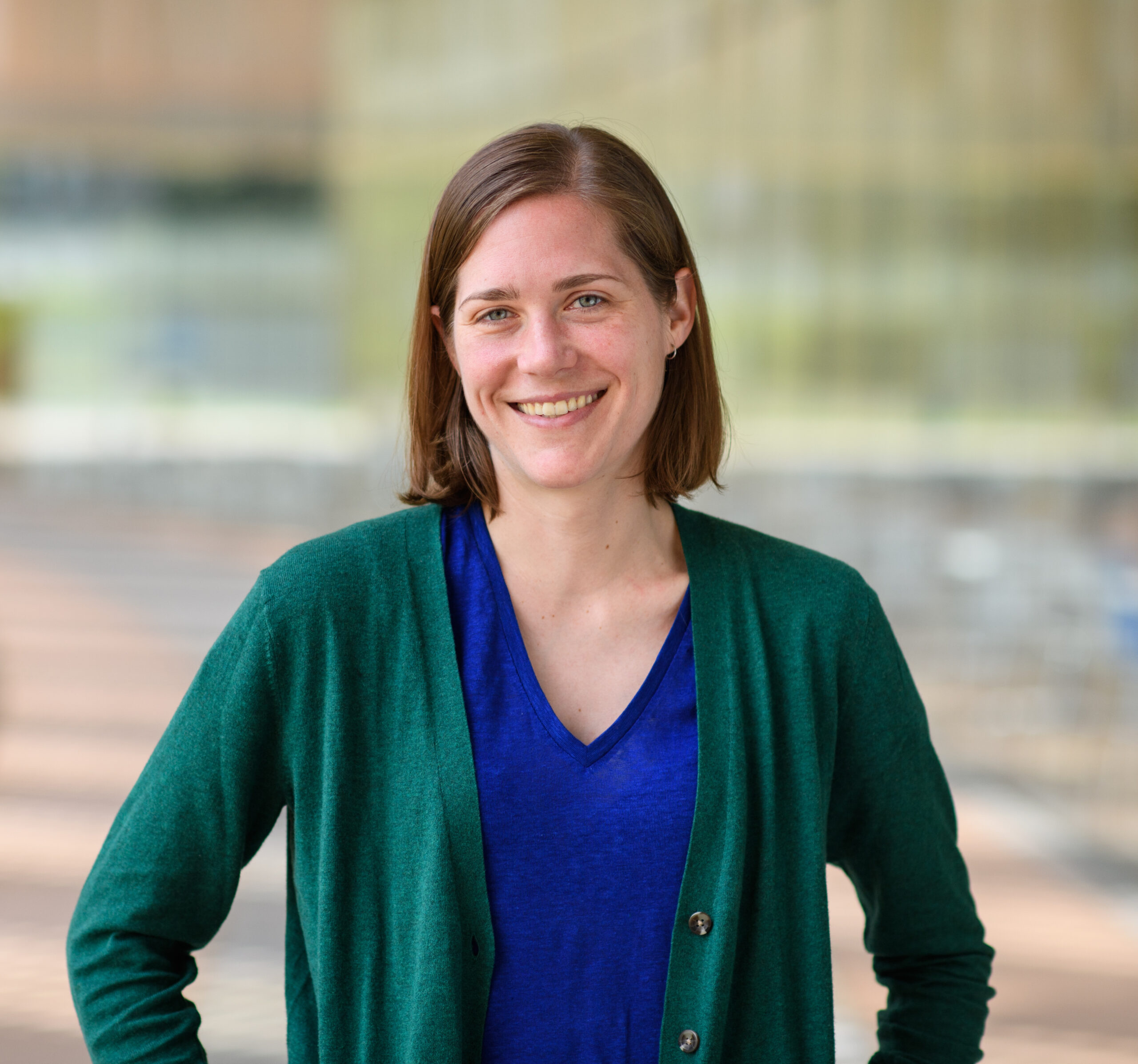 Amanda Lea in green jacket and blue shirt. Smiling with a blurry background