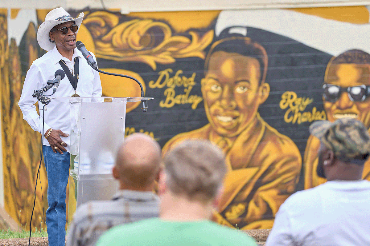 Carlos DeFord Bailey stood and spoke in front of his grandfather DeFord Bailey’s likeness in the “First Family of Black Country” mural