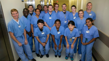 Pictured: A group of Vanderbilt Business students in scrubs standing in a hospital hallway. Students masters in healthcare