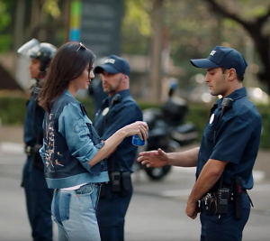 Pictured: A screenshot from the 2017 cringeworthy marketing campaign that Pepsi released with Kendall Jenner. Kendall Jenner is handing a police offer a Pepsi at a protest.