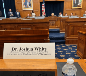Pictured: White's perspective at the hearing entitled “Reforming the Proxy Process to Safeguard Investor Interests.”. His name card reads "Dr. Joshua White, Assistant Professor of Finance at Vanderbilt University's Owen Graduate School of Management." The background of the photo shows the room where the hearing was located.
