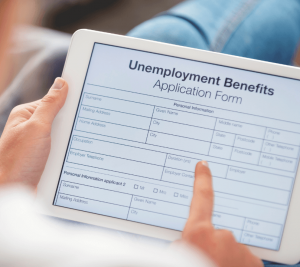 Pictured: A person is holding a tablet. The tablet is open on a screen with an unemployment benefits application form.