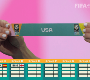 Pictured: A screenshot from the 2023 Women's World Cup Draw. The image shows hands holding a piece of paper that says "USA." 