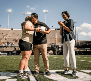 Pictured: Sarah Marvin and Mario Avila hug on the Vanderbilt football field as Candace Storey Lee claps with a huge smile. 