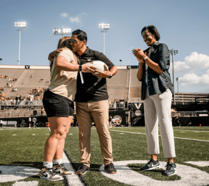 Pictured: Sarah Marvin and Mario Avila hug on the Vanderbilt football field as Candace Storey Lee claps with a huge smile.