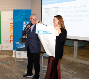 Pictured: Eric Thrailkill (left) and Haley Combs (right) show the event attendees a Project Healthcare t-shirt. The shirt is white with blue ink.