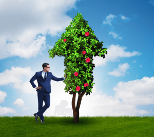 Pictured: Standing on green grass and in front of a blue sky with clouds, a business professional leans up against a tree that is shaped like an arrow pointing upward. The image represents an improvement in corporate sustainability. 