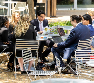 Pictured: 2023 Accelerator students are sitting at a table working together on the Nashville Superspeedway project. The students are sitting at an outdoor table at Vanderbilt Business' Management Hall.