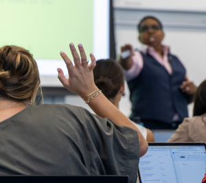 Pictured: Professor Jen Riley encourages student participation in her classes. This image shows a student is raising their hand in Riley's class. Riley is pointing toward the student to indicate it is their turn to speak.