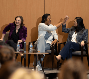 Pictured: Panelists at Vanderbilt Business’ Executive Women in Leadership: New Leadership Strategies for 2024 event. The 3 panelists are sitting on a stage. Allie Feiner is on the left, Candice Storey Lee is in the middle, and Jennifer Hutcheson is on the right. Feiner is laughing, Lee and Hutcheson are giving each other a high five.