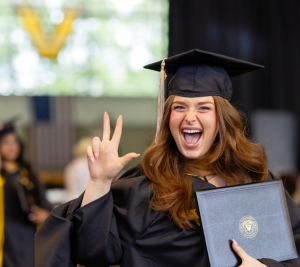 Pictured: Shanna Adam (MMark'24) is in her graduation regalia. She is smiling big and throwing up the "Anchor Down" hand-sign while holding her diploma.