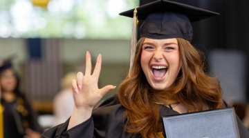 Pictured: Shanna Adam (MMark'24) is in her graduation regalia. She is smiling big and throwing up the "Anchor Down" hand-sign.