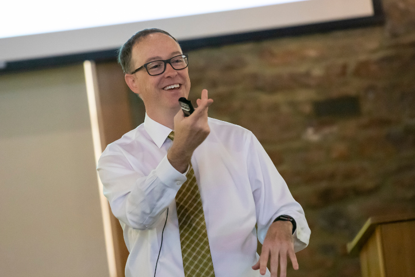 Pictured: Professor Josh White engages with his students at Vanderbilt Business to teach complex finance topics. He uses instances like the Reddit IPO case to enhance learning. In this photo, he is standing at the front of a classroom, smiling and pointing to a student. The student is not in the frame of the picture, but they are raising their hand to speak.