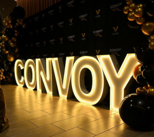 Pictured: LED neon letters spell out "Convoy" under a gold and black balloon arch. The Convoy Conference display was set up in the lobby of Management Hall at Vanderbilt Business.