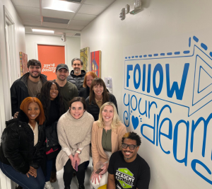 Pictured: Thomas Kelly and Vanderbilt Business students gather for a photo with a mural that says "follow your dreams"
