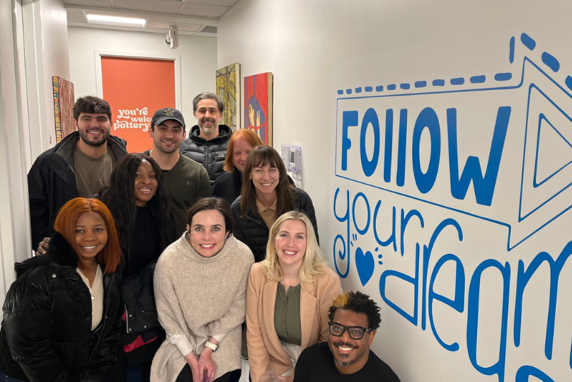 Pictured: Thomas Kelly and Vanderbilt Business students gather for a photo with a mural that says "follow your dreams"