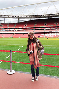 Yining Ding standing in Liverpool soccer stadium with the field and empty stands behind her