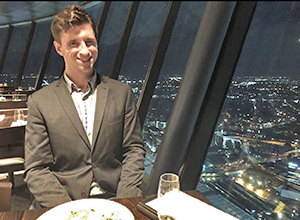 Devon Akers sitting at a table in a restaurant with a window and night view of a city in the background