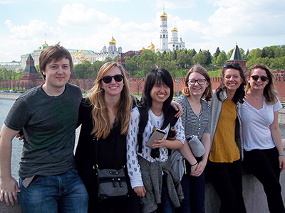 Six students leaning against a wall in a Russian city with a river and gold-domed towers and buildings in the background