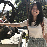 Bonnie Pang standing next to a bronze statue of a bull with trees in the background