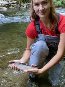 Woman smiling holding fish in stream