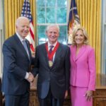 Jon Meacham with a medal around his neck shaking hands with President Joseph R Biden and First Lady Jill Biden