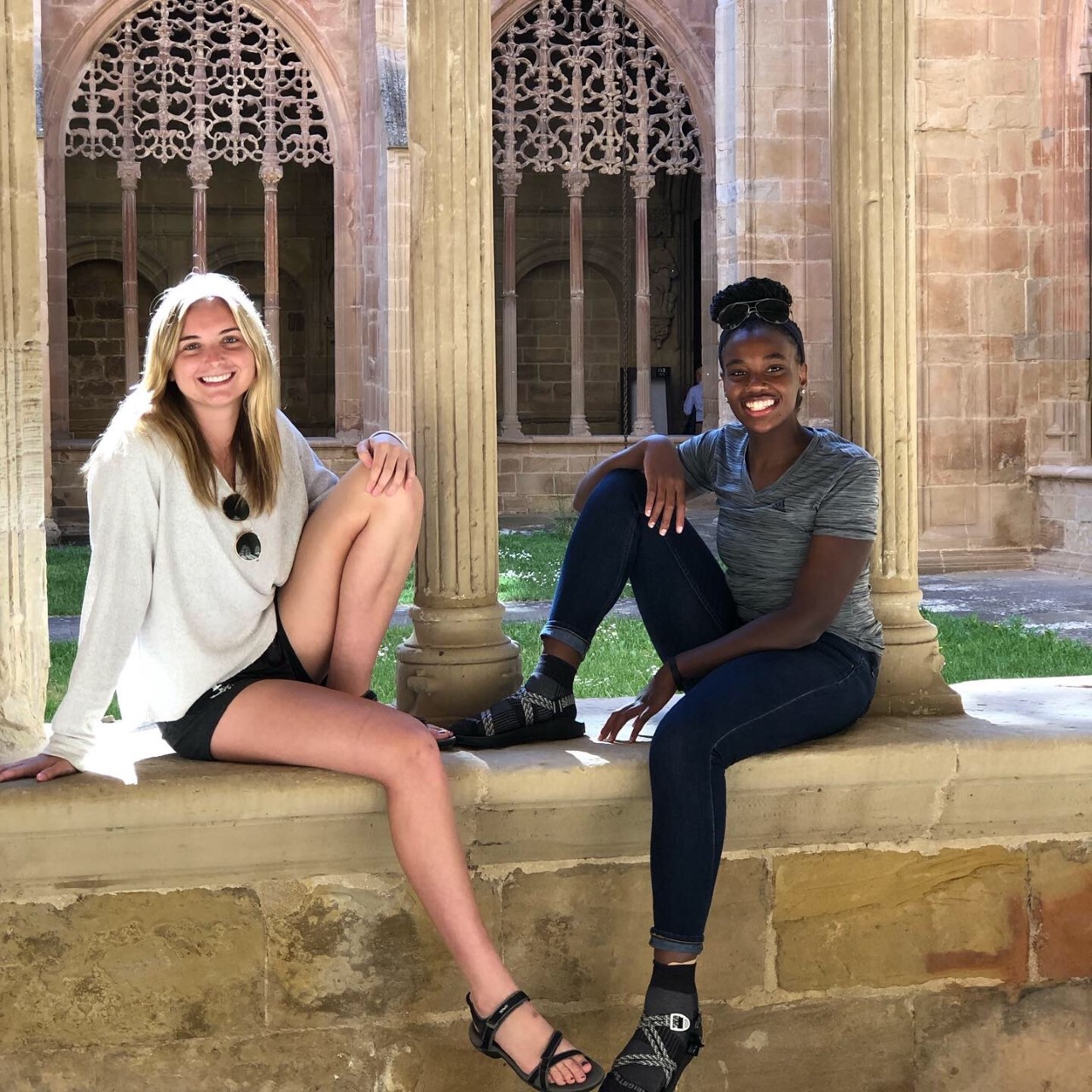 Two smiling women sitting on a stone wall.