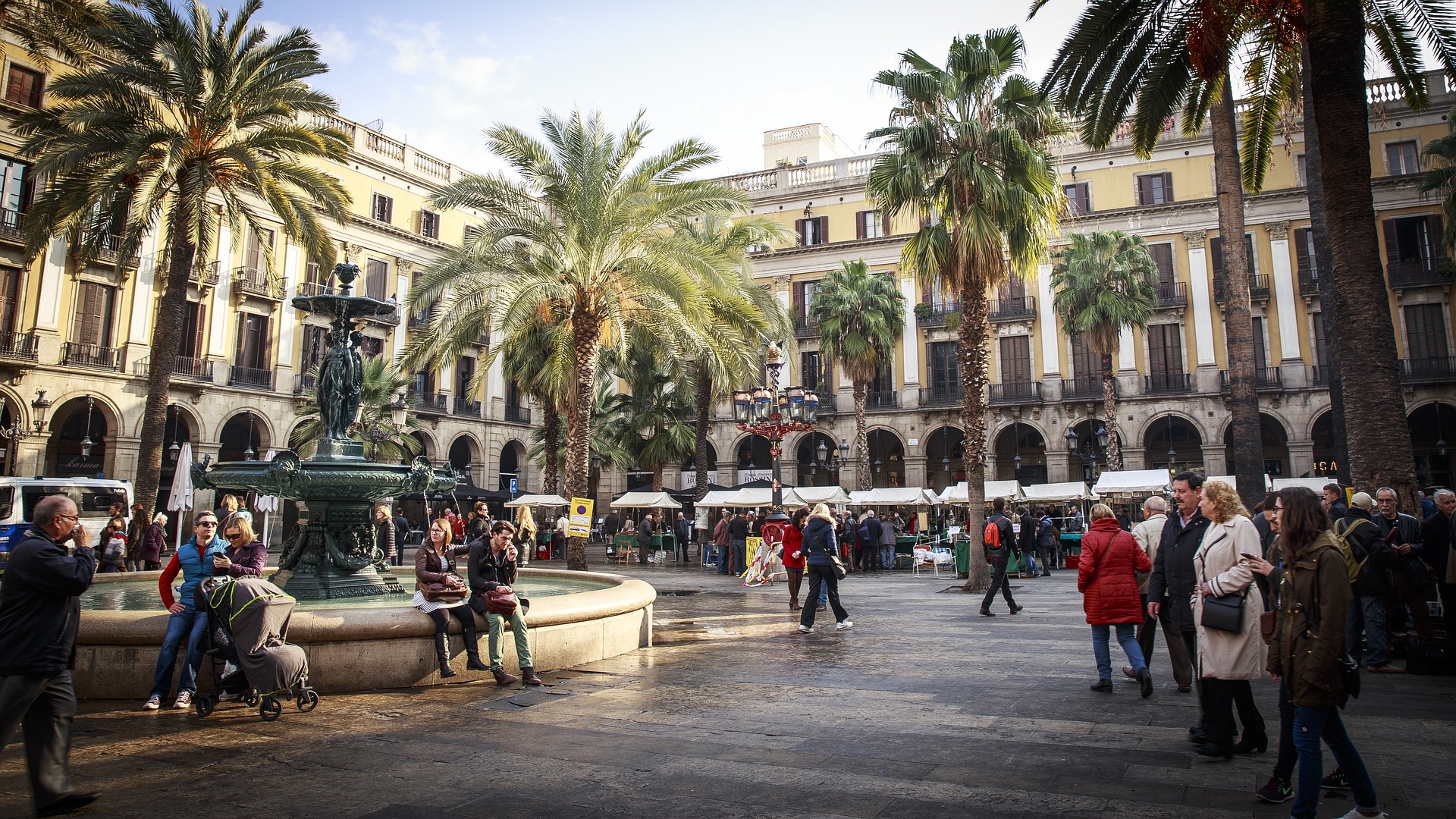 Busy market area with a fountain and many people walking.