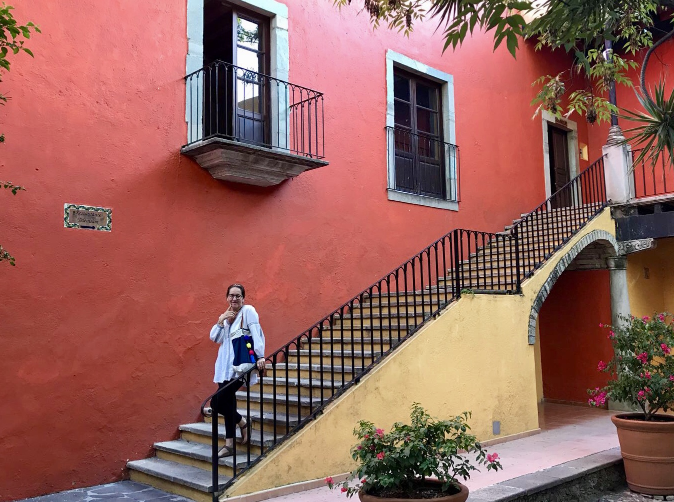 A woman posing on stairs in front of a bright red wall.