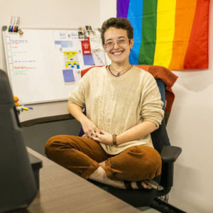 Cassidy Parkison sitting at a desk in front of a white board and rainbow flag