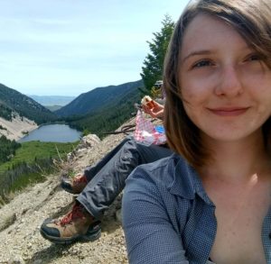 Sarah Williams takes a selfie on the side of a mountain overlooking a body of water