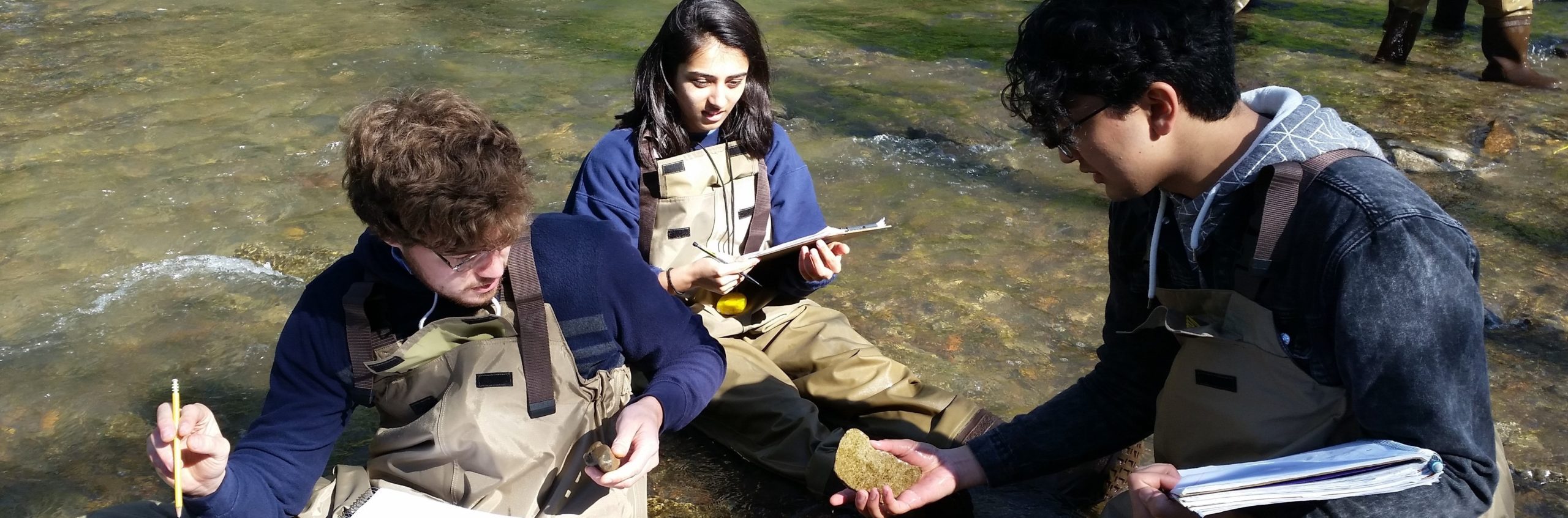 EES students sit in a stream while examining a rock