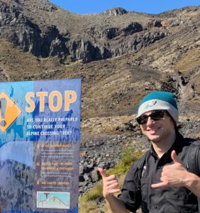 Liam Kelly standing beside a sign for the Alpine Crossing Trek