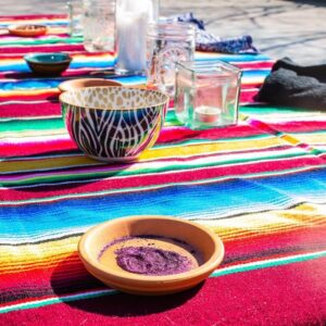 Glitter Ashes in a small terra cotta dish. They are on a woven blanket of rainbow colors in the sun. There are candles and other bowls in the background.