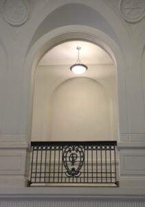 Ornate railings with the letter "P" encase the hallways connecting to the stairway.
