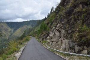 View of cloudy skies and a rocky slope with a paved road running through the image.