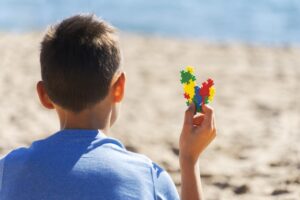boy-sitting-beach-looking-sea-ocean-holding-colorful-autism-awareness-heart_206881-381