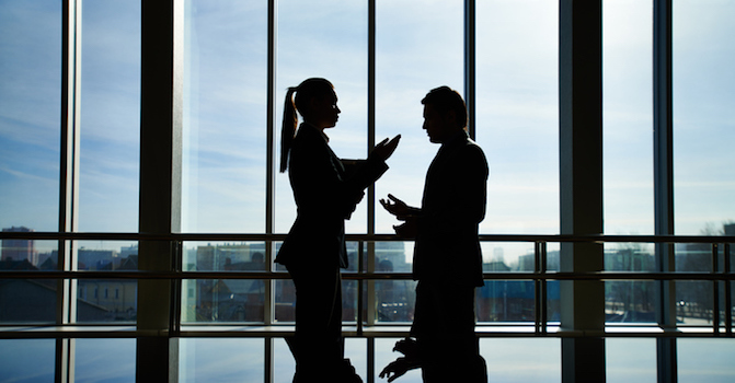 Silhouettes of businessman and businesswoman arguing standing by railing